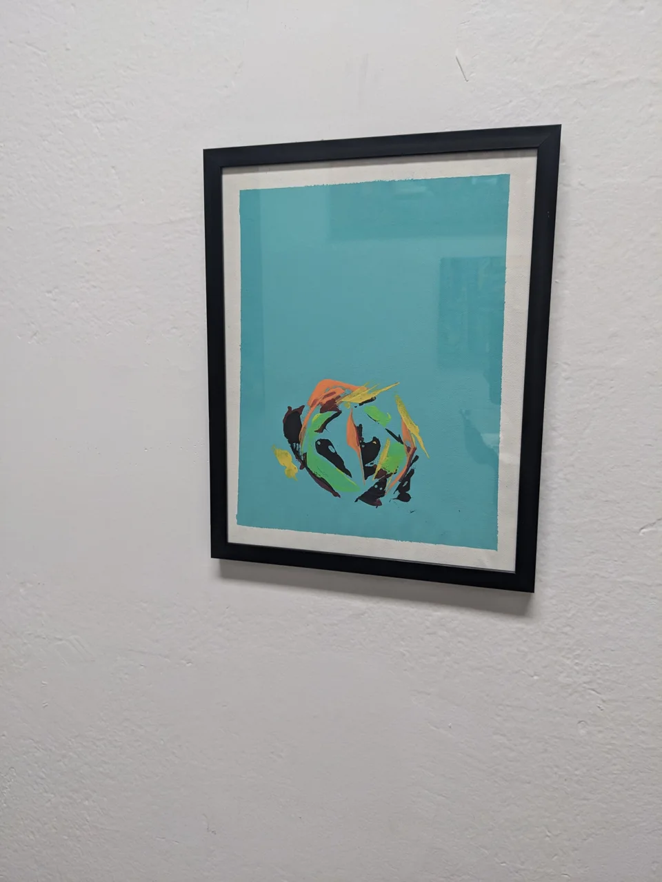 Under a black frame, a flat teal-blue ground holds one small, fast cluster of paint just below center. The marks are